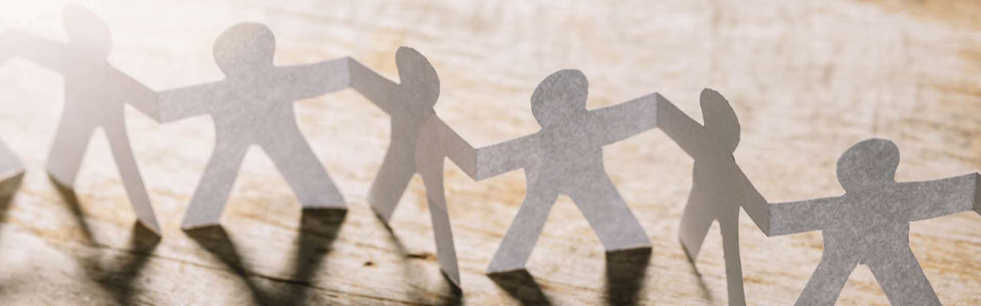 Papiermännchen, die einander festhalten vor einem Holzhintergrund.